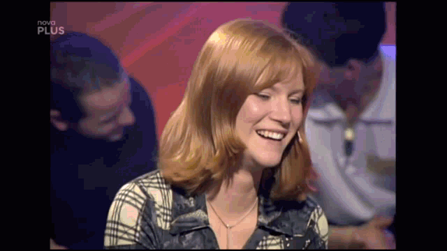 a woman with red hair is smiling in front of a nova plus screen