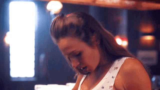 a woman in a white tank top is standing in a dark room
