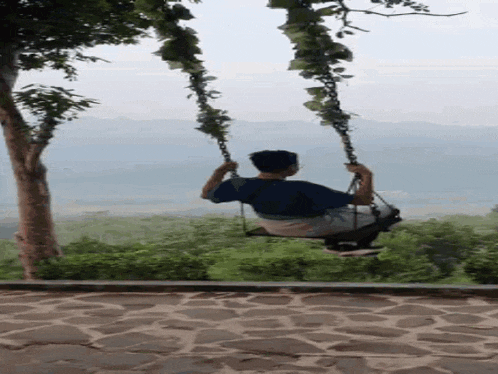 a man is sitting on a swing with a view of the mountains behind him .