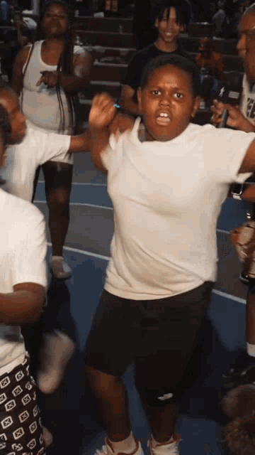 a boy in a white shirt and black shorts is dancing with a group of people