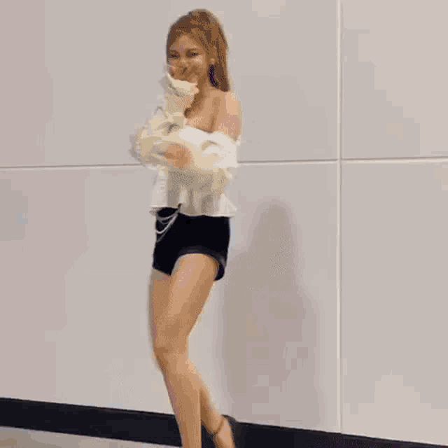 a woman is dancing in a room wearing shorts and a white top .