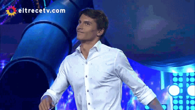 a man in a white shirt stands in front of an eltrecetv.com advertisement