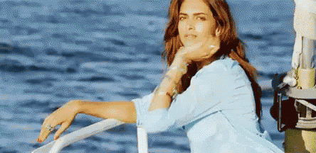 a woman is sitting on a boat in the ocean with her hand on her chin .