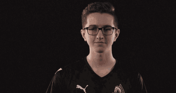 a young man wearing glasses and a black puma shirt holds his hand up to his ear