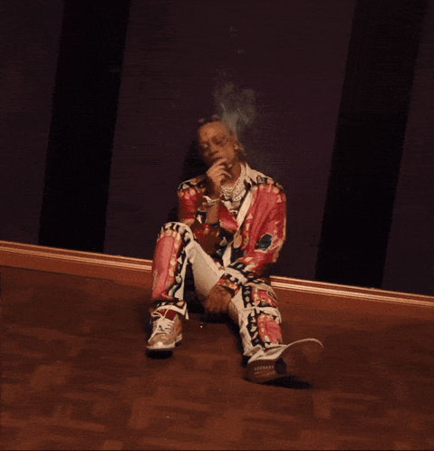a man in a colorful outfit sits on the floor smoking