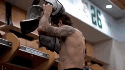a shirtless man is standing in a locker room holding a bag .