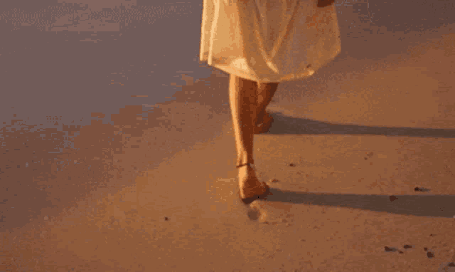 a woman in a white dress is walking on a beach
