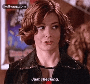 a woman in a denim jacket is saying `` just checking '' while looking at the camera .