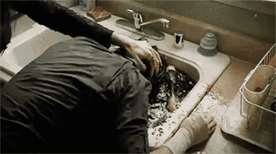 a man is laying in a sink with his head in the sink .