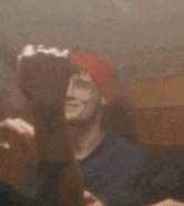 a man in a red hat is taking a selfie with another man in a dark room .