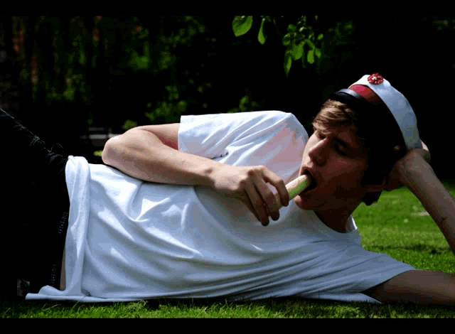 a young man laying on the grass eating a strawberry