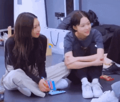 two girls are sitting on the floor talking to each other and playing a game .