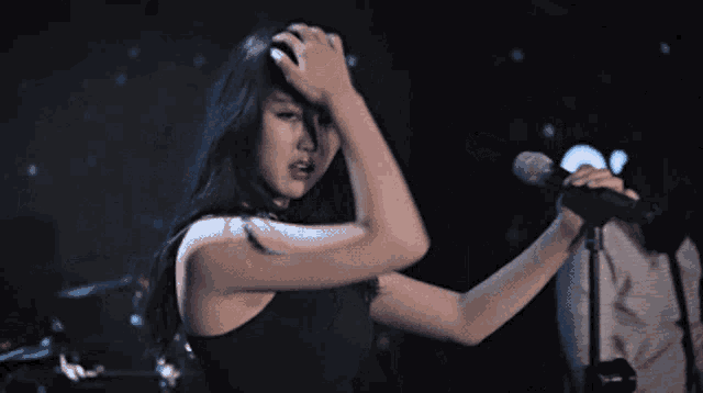 a woman singing into a microphone with her hands on her head