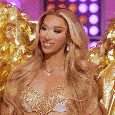 a woman with long blonde hair is smiling and wearing a gold bra