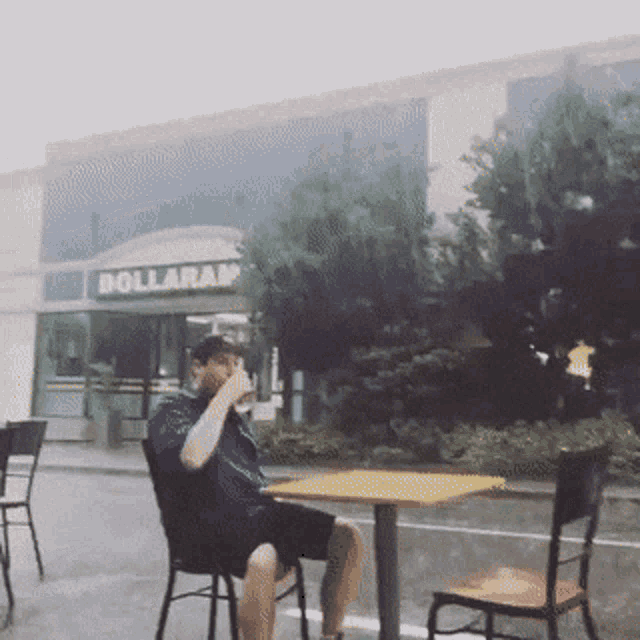 a man sits at a table outside of a dollarama store