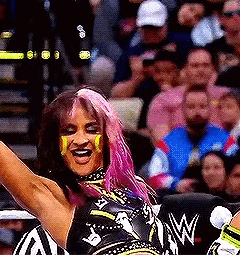 a woman with pink hair is wrestling in front of a crowd of people .
