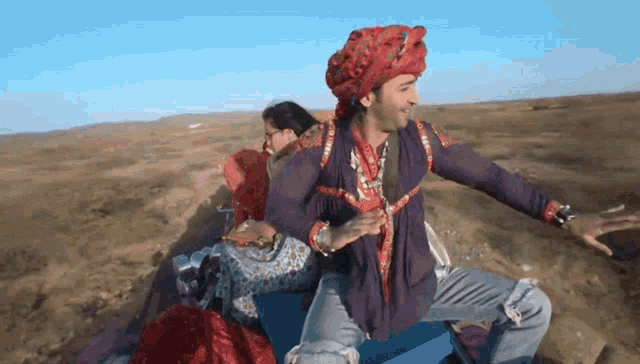 a man wearing a turban and a purple shirt is sitting on a blue box