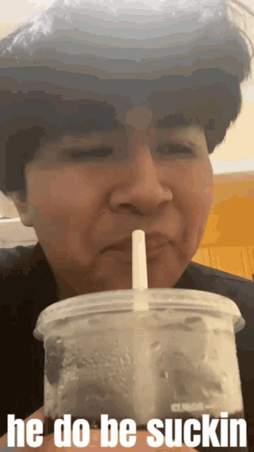 a man is drinking from a plastic cup with a straw and says he do be suckin