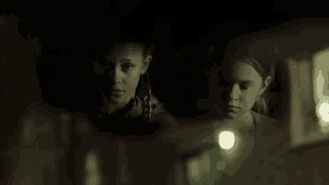 two young girls are looking at something in a mirror in the dark .