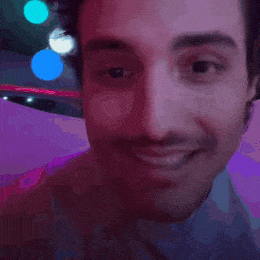 a close up of a man 's face in a dark room with purple lights behind him