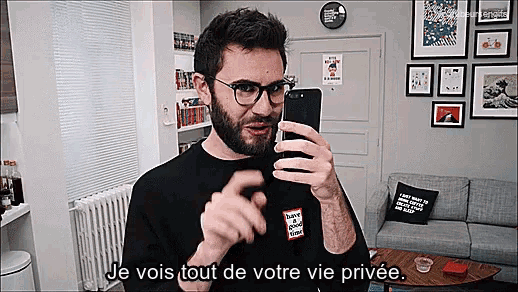 a man with glasses is taking a selfie in a living room with the words je vois tout de votre vie privée