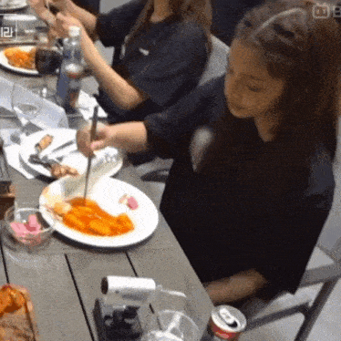 a woman is sitting at a table with a plate of food and a can of soda