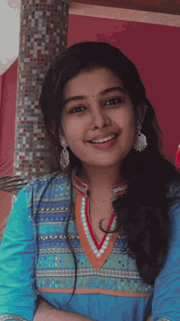 a woman wearing a blue shirt and earrings smiles