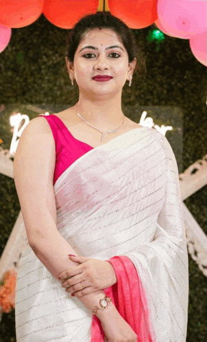 a woman in a white saree and a pink blouse stands in front of balloons and a sign that says love