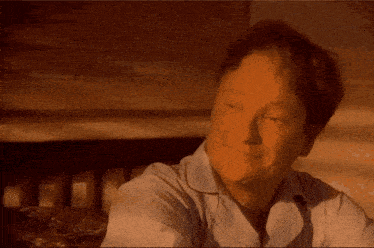 a man in a white shirt is smiling while sitting in front of a bed