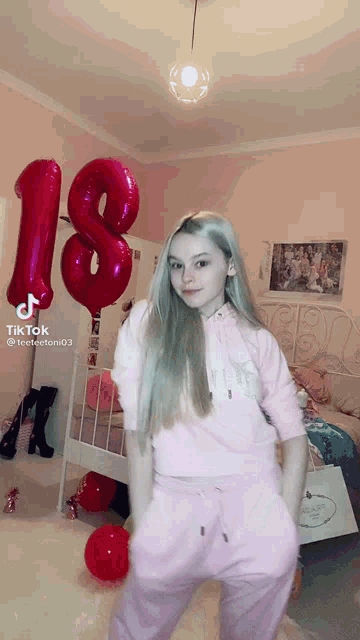 a girl in a pink outfit is dancing in front of red balloons with the number 18 on them