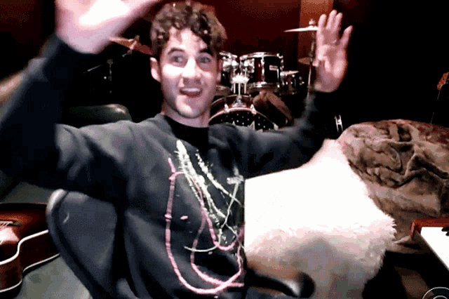a man sitting in front of a drum set with his hands up
