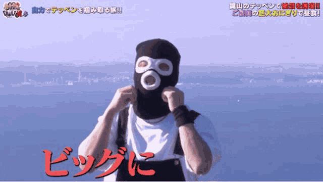 a man wearing a black mask with white circles on his eyes stands in front of a body of water