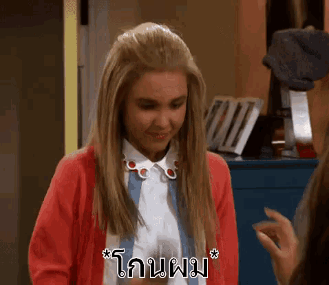 a woman wearing a red cardigan and a white shirt is talking to another woman in thai .