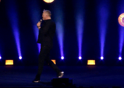 a man singing into a microphone with the words very nice behind him