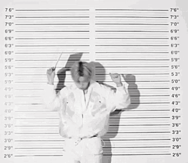 a man in a white jacket is standing in front of a police line up showing his height at 7 ' 3 "