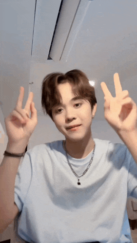 a young man in a blue shirt is making a peace sign with both hands