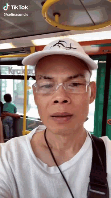 a man wearing glasses and a hat is taking a selfie on a bus with tiktok written above him