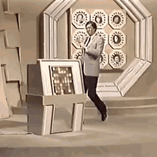 a man in a suit and tie is standing in front of a computer in a room .