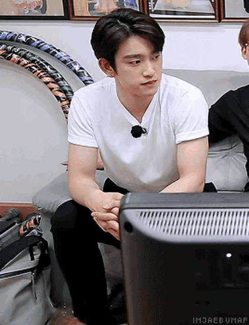 a man in a white shirt is sitting on a couch looking at a television
