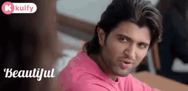 a man in a pink shirt is sitting at a table and looking at the camera with the words beautiful behind him .