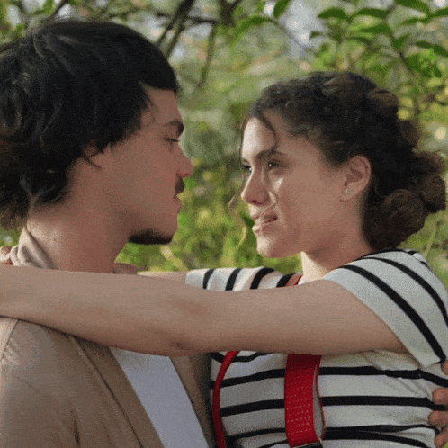 a woman in a striped shirt is hugging a man in a tan cardigan
