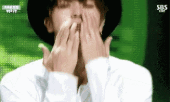 a man is covering his mouth with his hands while wearing a hat .