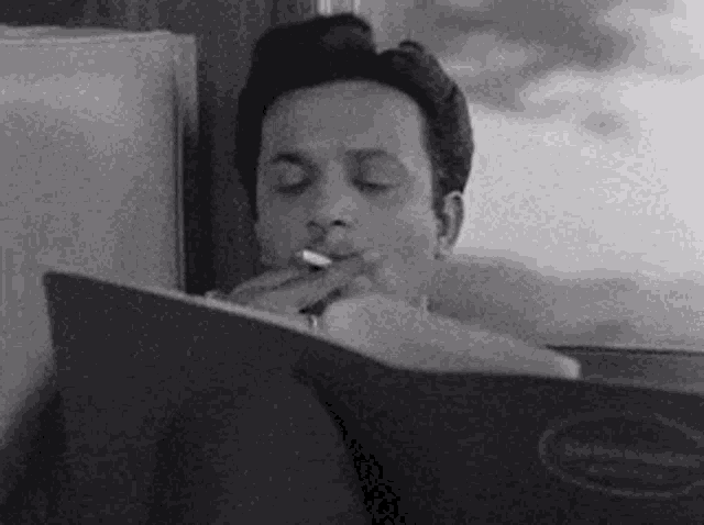 a man is reading a book while smoking a cigarette .