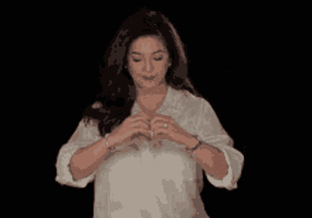 a woman in a white shirt is making a heart with her hands