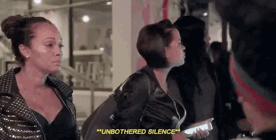 two women are standing next to each other and one of them is saying `` unbothered silence '' while holding a cell phone .