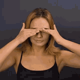 a woman in a black tank top covering her eyes with her hands .