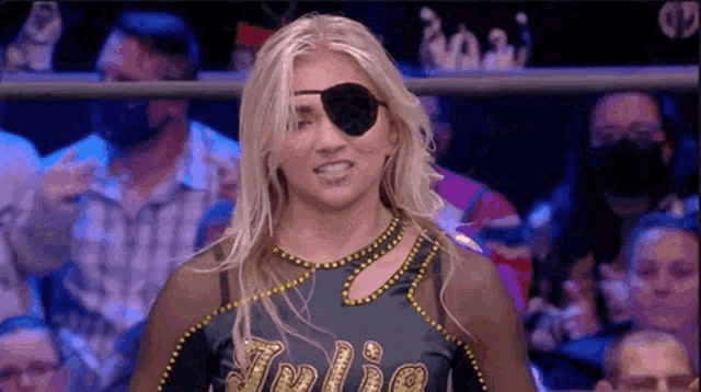 a woman wearing a eye patch is standing in front of a crowd at a wrestling match .