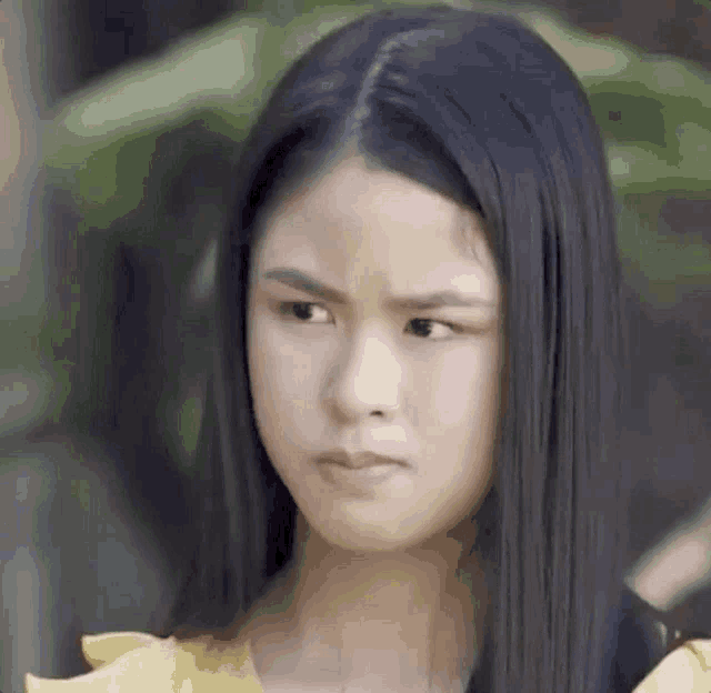 a young woman with long black hair is making a funny face and wearing a yellow shirt .