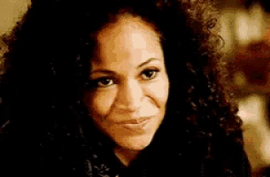 a woman with curly hair is smiling at the camera .