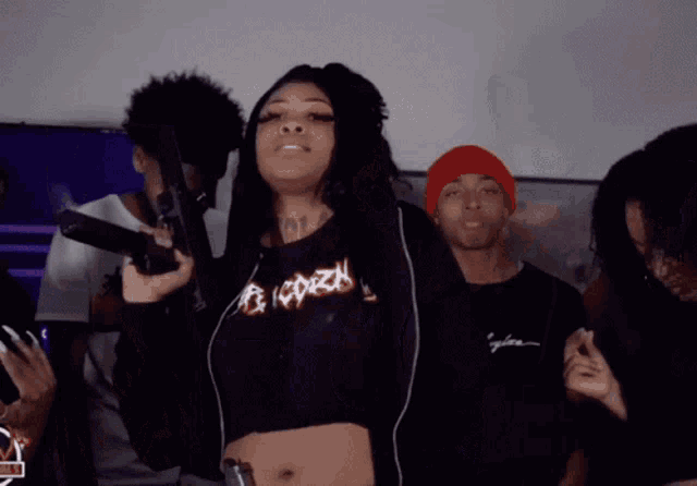 a woman in a black crop top is holding a gun in front of a group of people .